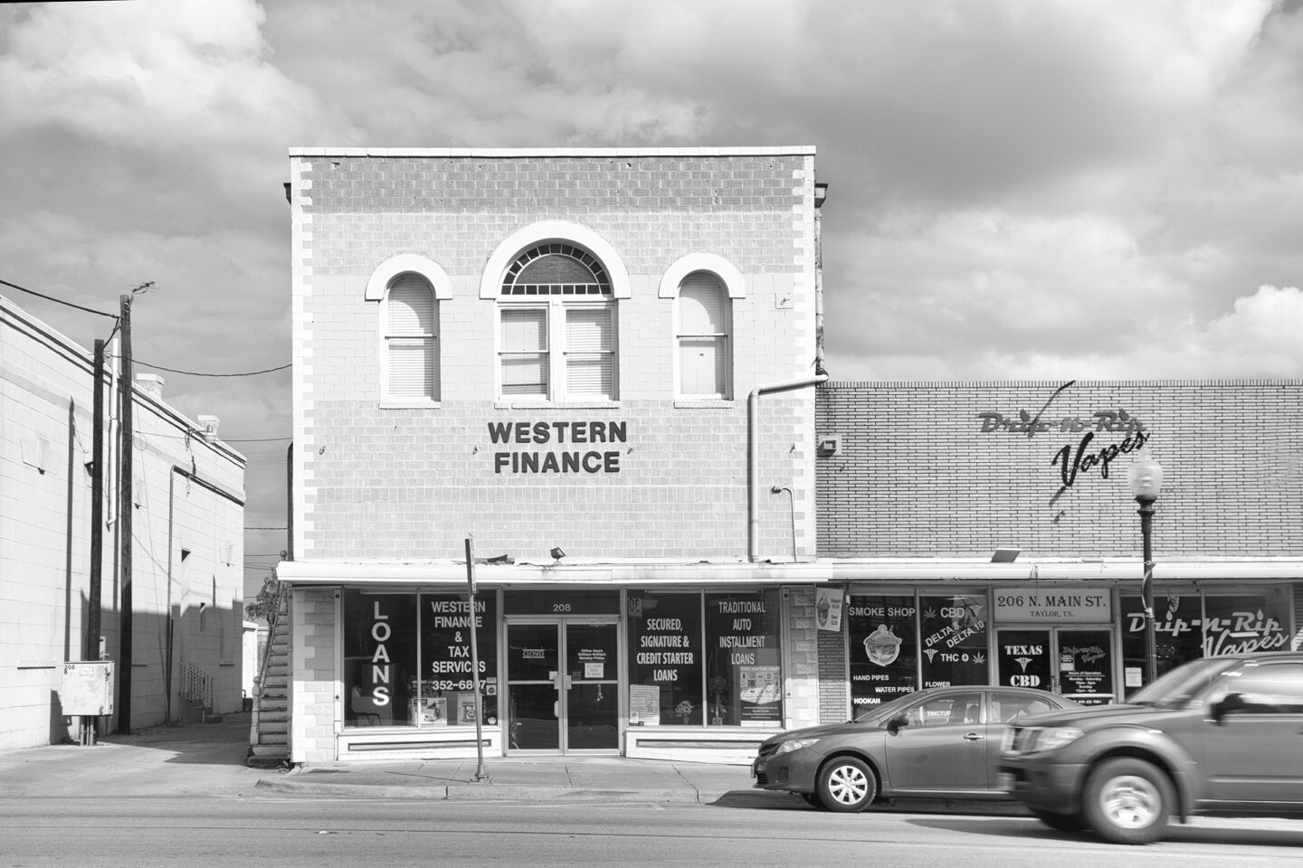 Monochrome image of rural Taylor, Texas town featuring Western Finance business with cars going past, by Carol Schiraldi 