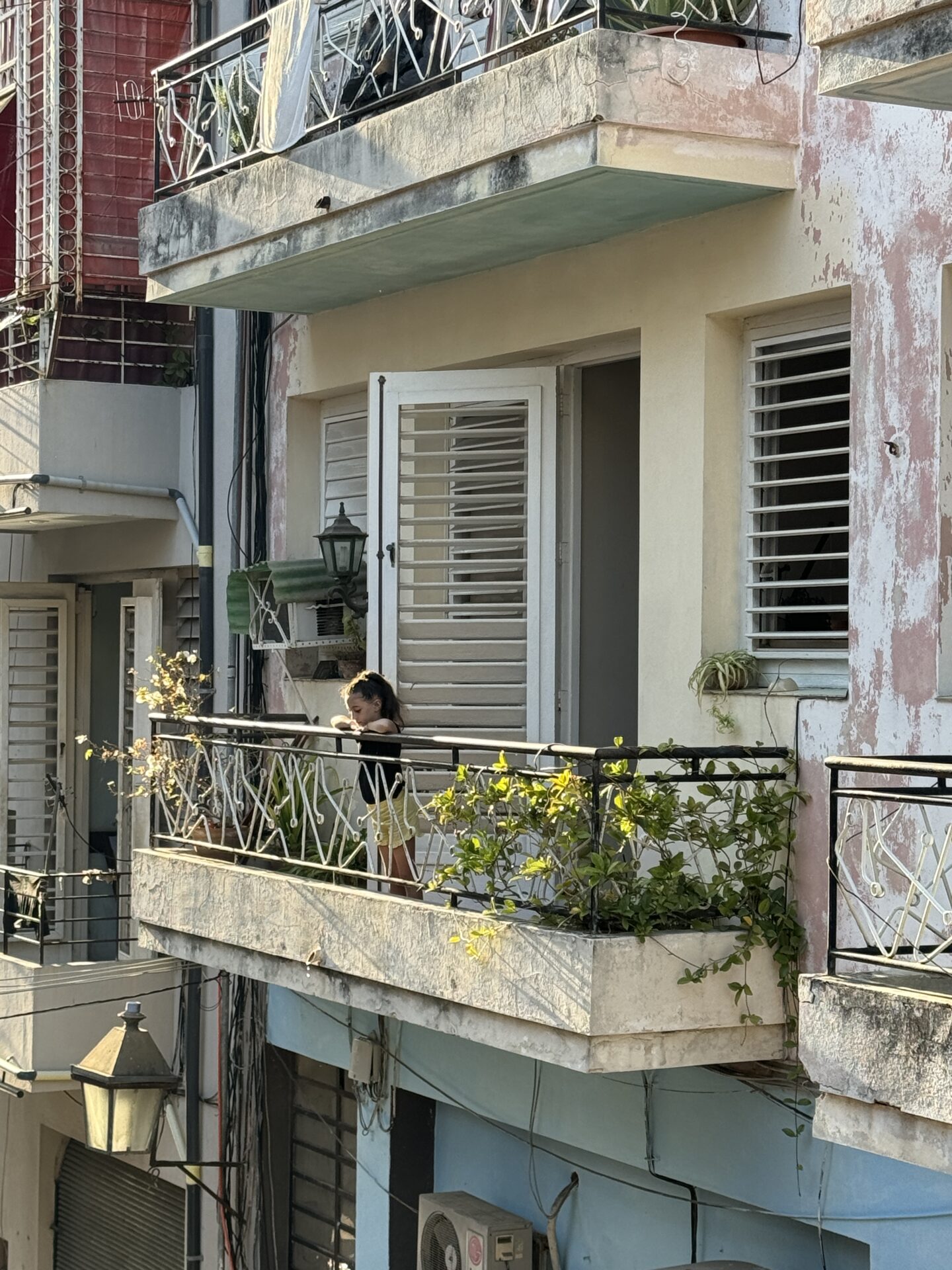 A girl standing on a balcony in Old Havana looking down on the street, image by Carol Schiraldi of Carol's Little World. 