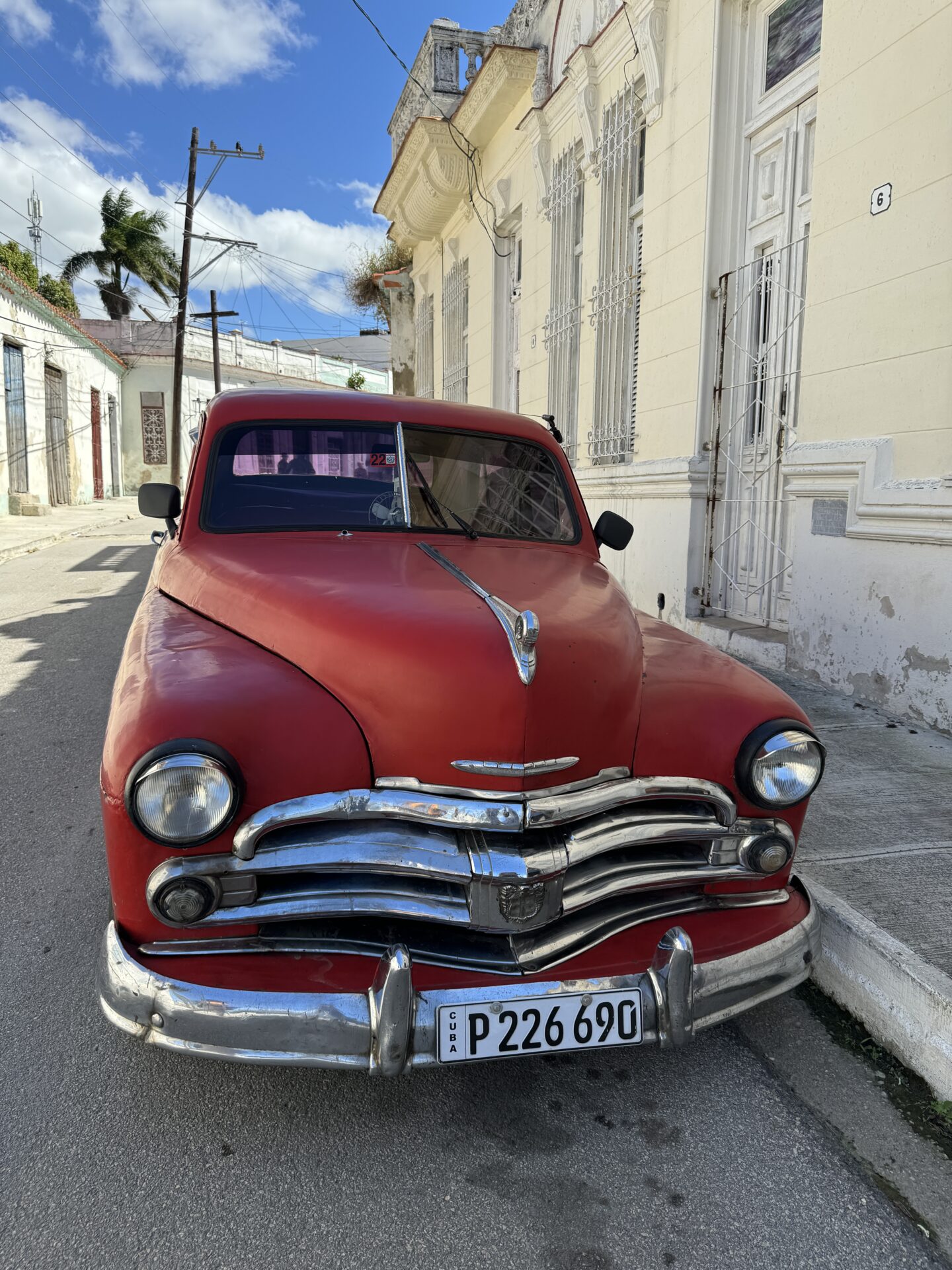 Large red classic automobile set against backdrop of Regla neighborhood in Havana, Cuba, by Carol Schiraldi of Carol's Little World 