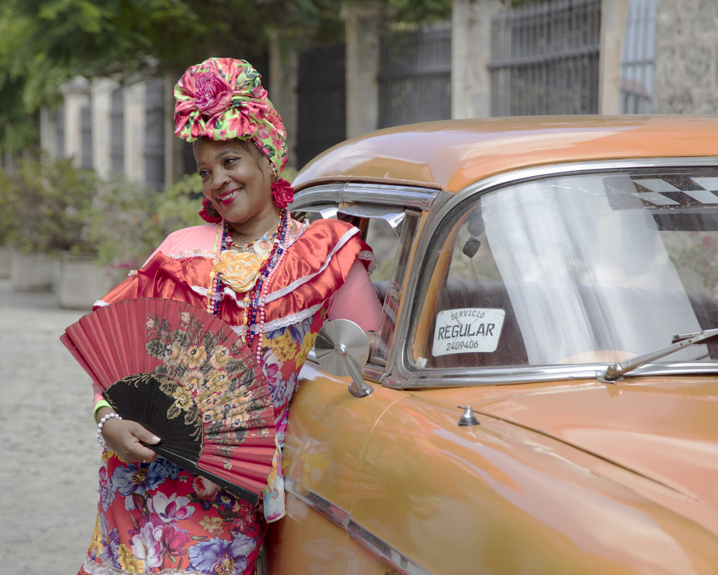 A portrait from Cuba featuring a colorful dancer next to a taxi cab.
