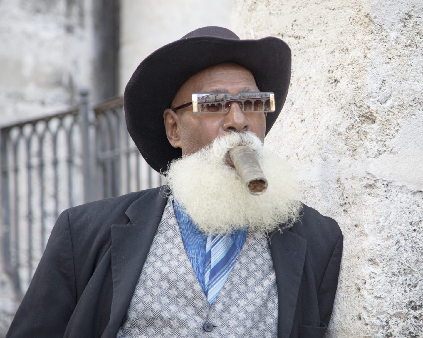 A portrait from Cuba featuring Willie de Cuba smoking a cigar wearing a cowboy had a wild sunglasses.