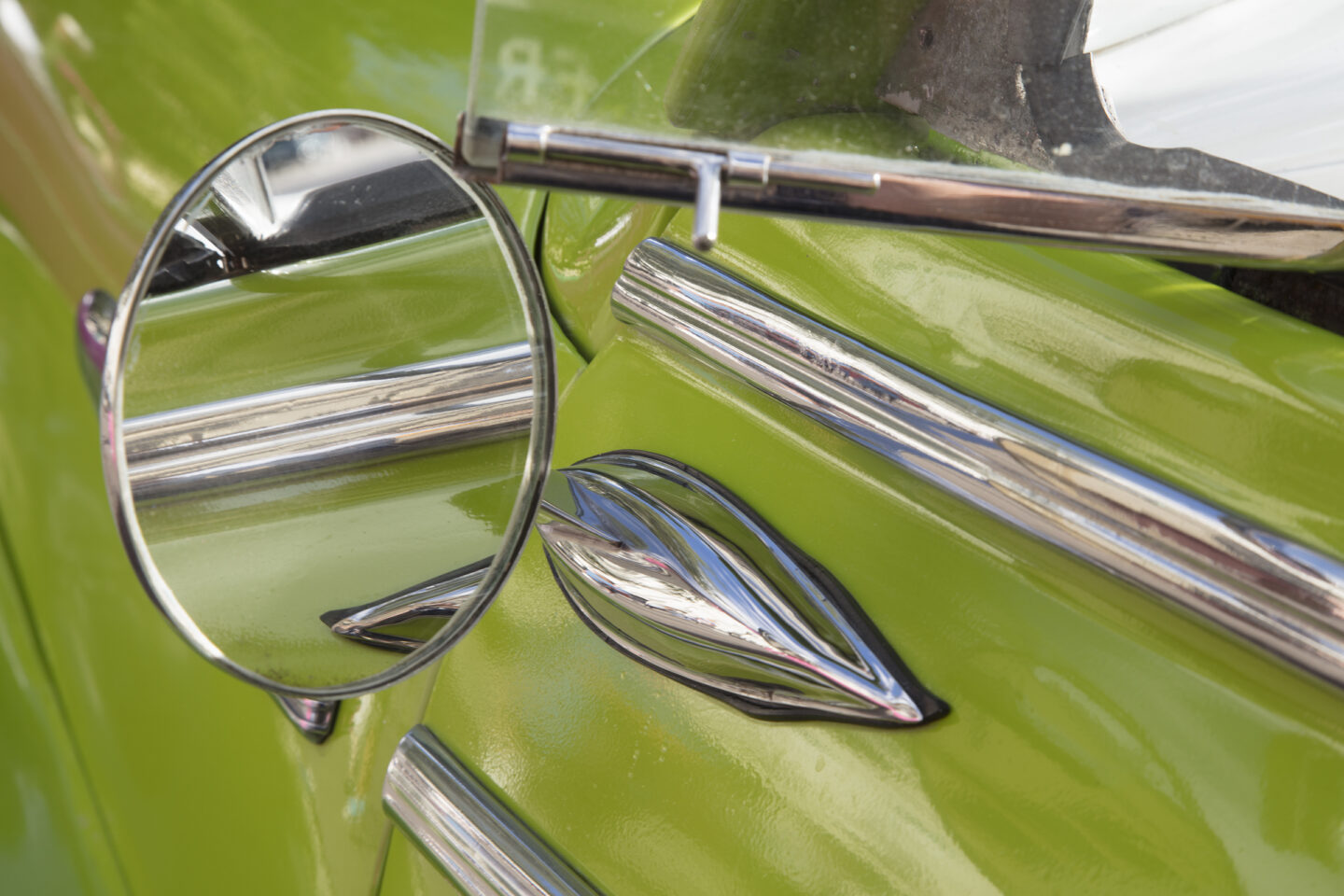 Close up almost abstract view of a car that is bright green in color with details of the rear view mirror. 